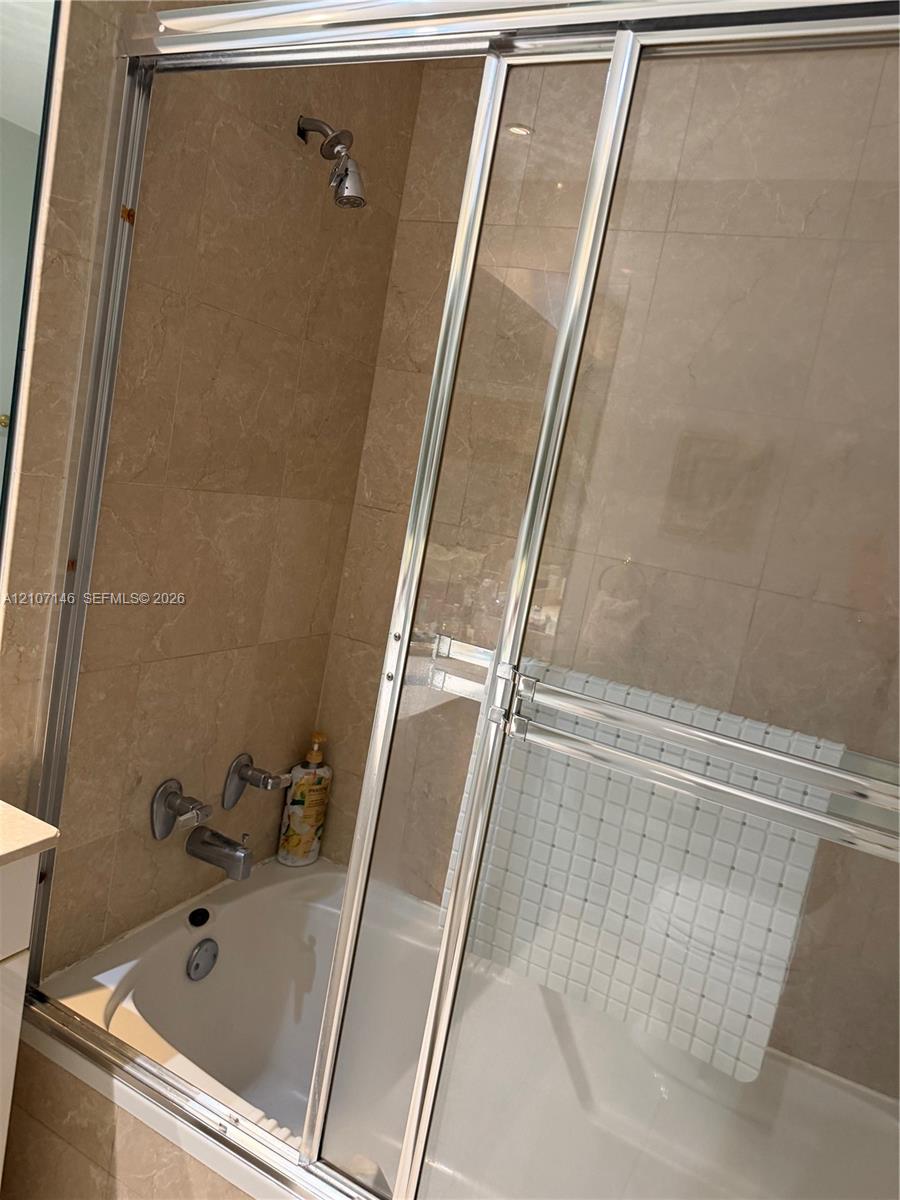 Shower and bathtub combination featuring full-height neutral-toned stone tile surround, chrome sliding glass doors, and a wall-mounted chrome faucet assembly