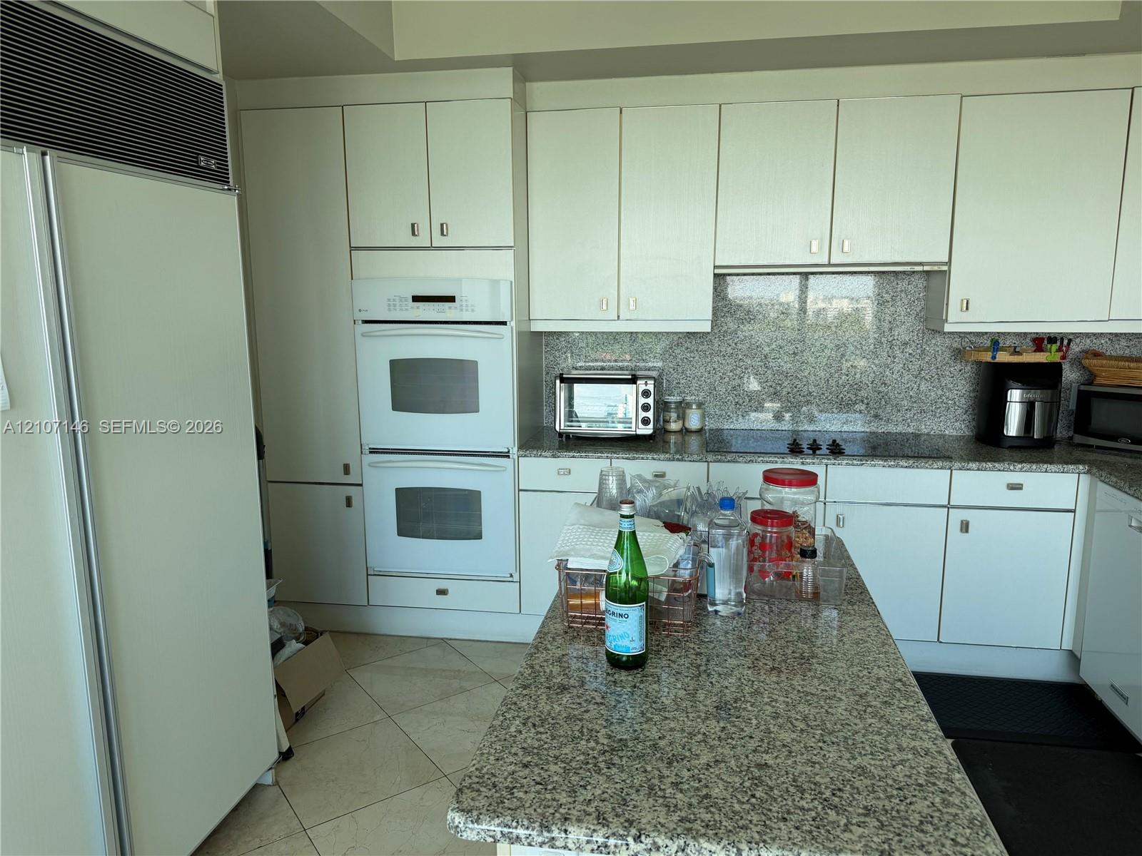 Kitchen featuring white cabinetry, stone countertops, stone backsplash, integrated double oven, and integrated refrigerator