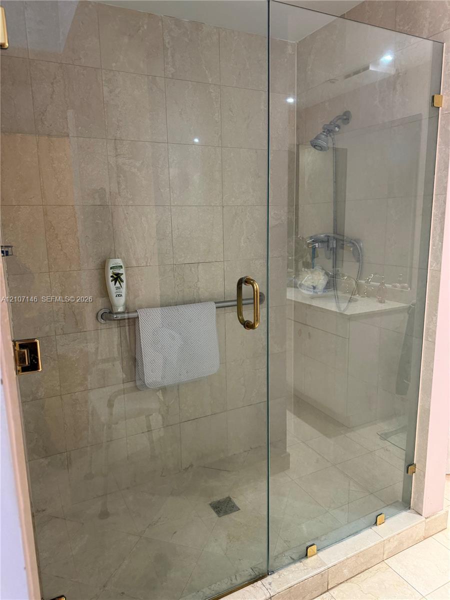 Walk-in shower enclosure featuring floor-to-ceiling tile, frameless glass door, metallic hardware, and wall-mounted shower fixture