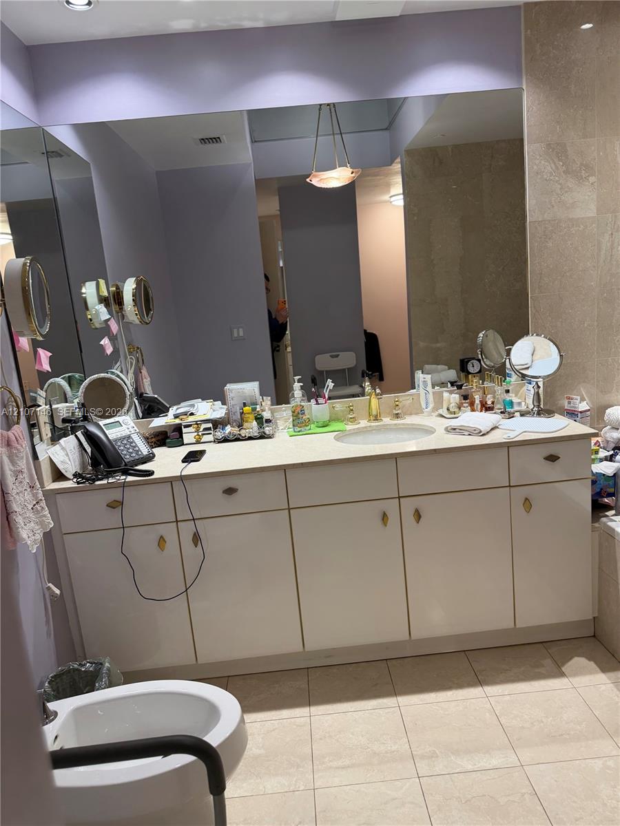 Bathroom vanity featuring a light-toned countertop, integrated oval sink, extensive white cabinetry, large wall-mounted mirror, and tile flooring