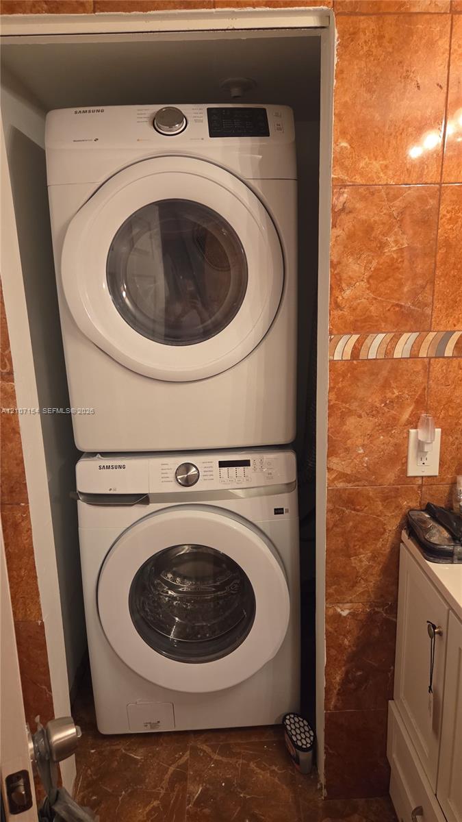 Stacked front-loading washer and dryer unit, set within a dedicated recessed laundry alcove featuring tile wall finishes and decorative border accents