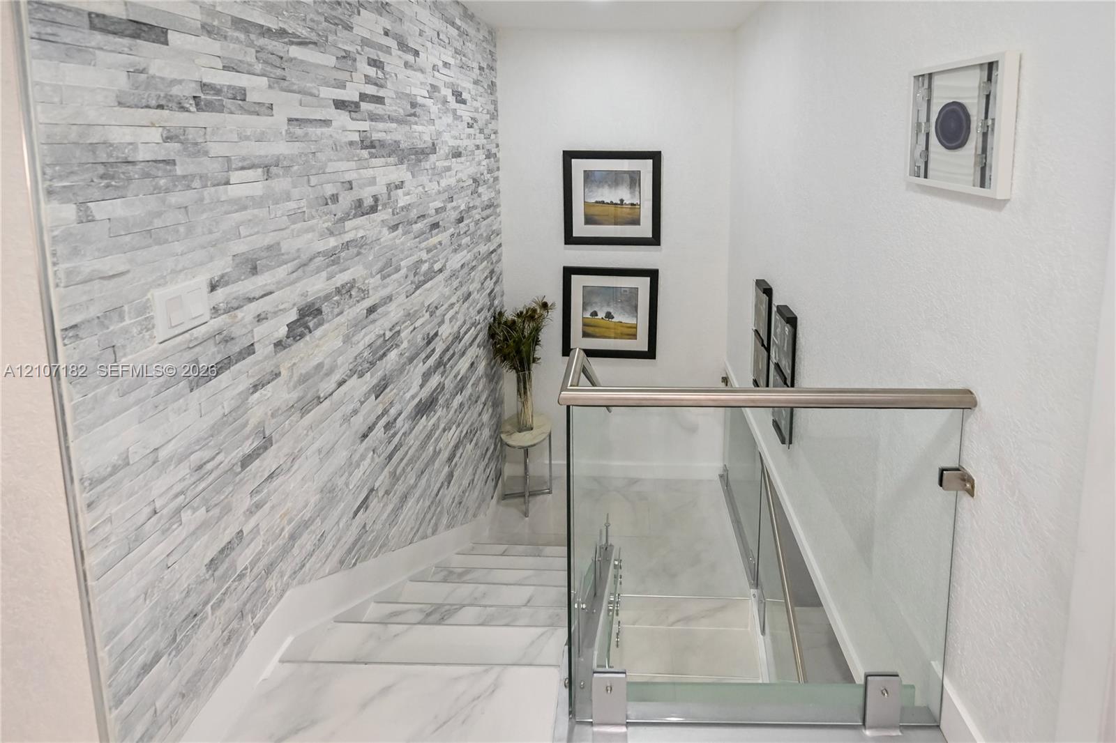 Staircase featuring stacked stone accent wall, large-format tile flooring, and glass panel railing with a metallic handrail