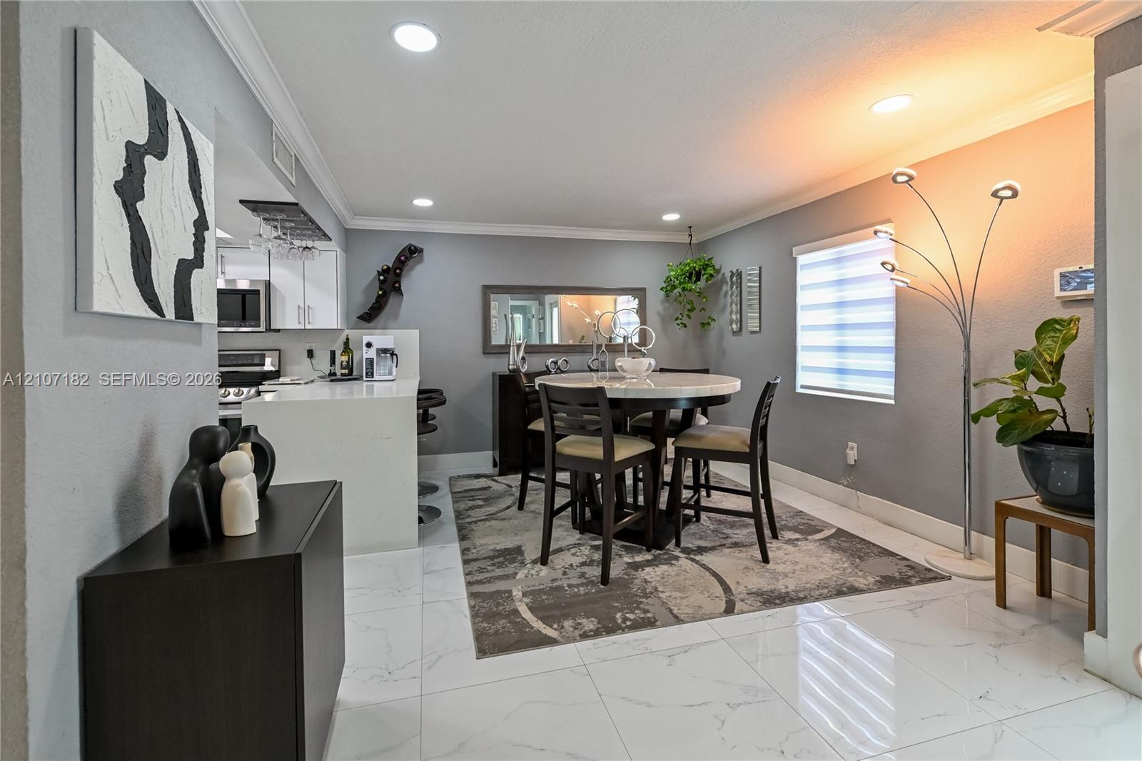 Large-format tile flooring, recessed lighting, crown molding, and a kitchen island with a light-toned countertop Large-format tile flooring, recessed lighting, crown molding, and a kitchen island with a light-toned countertop
