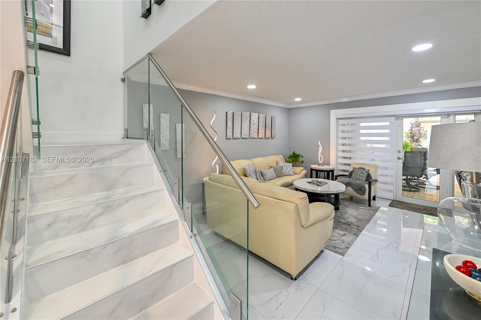 Staircase featuring stone-finish treads and a frameless glass railing with a metallic handrail, complemented by large-format polished tile flooring and recessed ceiling lighting