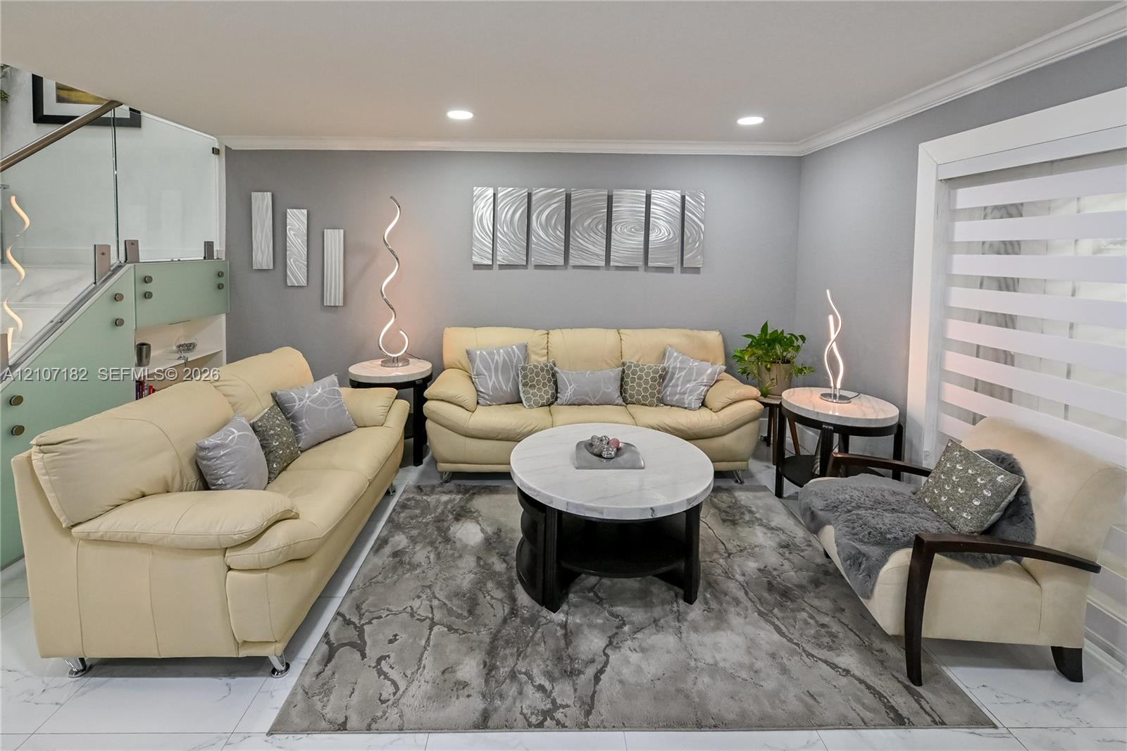 Living area featuring polished tile flooring, recessed lighting, and a staircase with glass panel railing