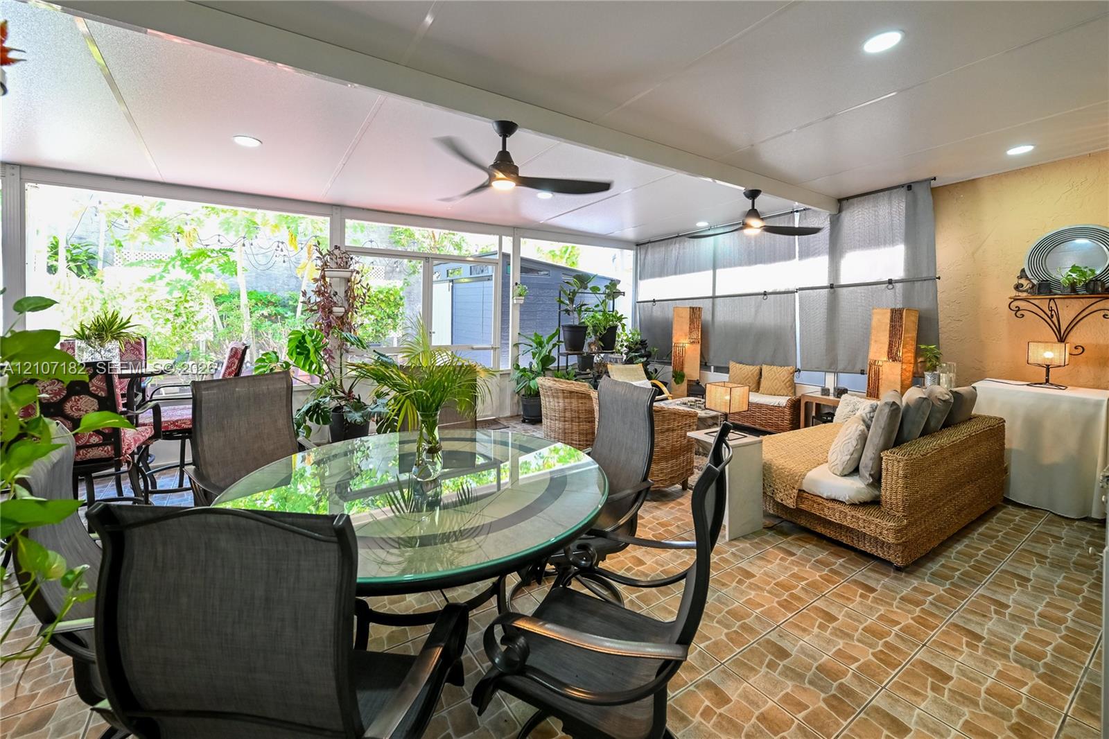 Enclosed patio featuring stone-pattern flooring, integrated ceiling lighting, dual ceiling fans, and expansive glass pane enclosures