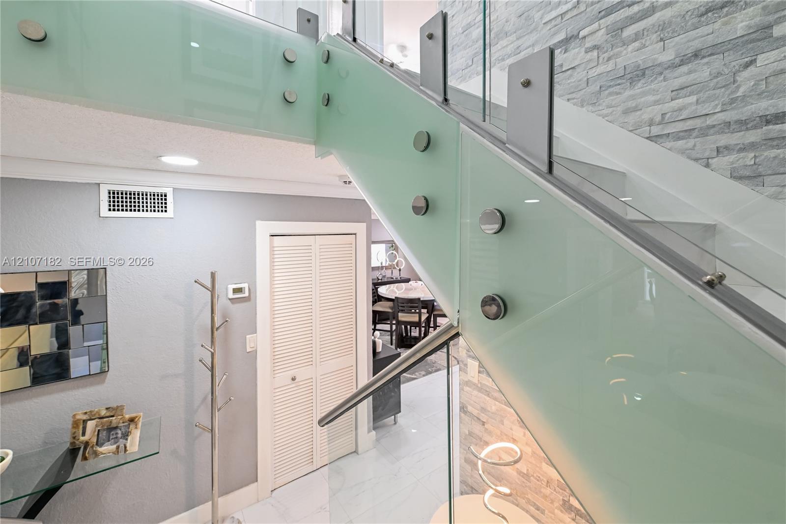 Staircase featuring frosted glass railings, brushed metal hardware, and a stacked stone accent wall with polished large-format tile flooring