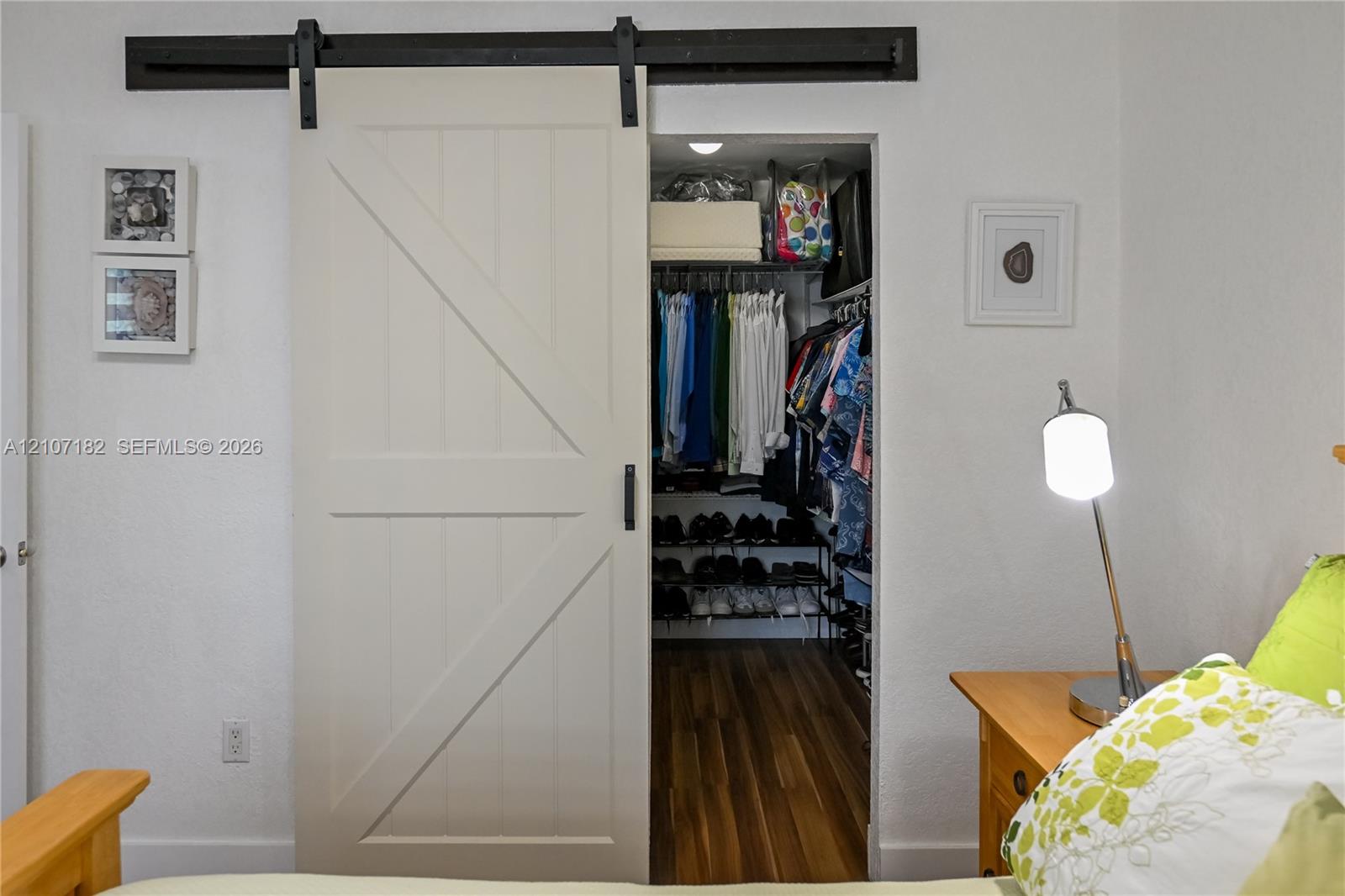 Off-white sliding barn door with matte black hardware and wood-finish flooring in the walk-in closet