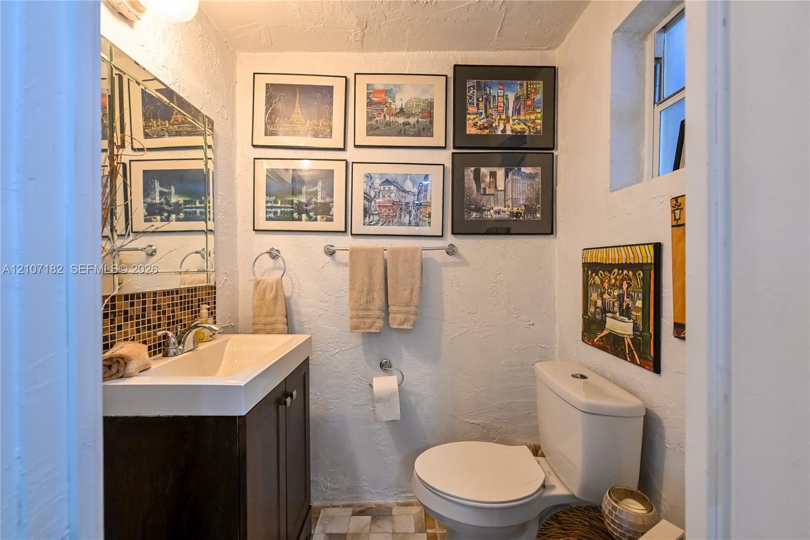 Bathroom featuring a vanity with an integrated sink, polished chrome faucet, mosaic tile backsplash, textured wall finish, and a large mirror with a decorative border