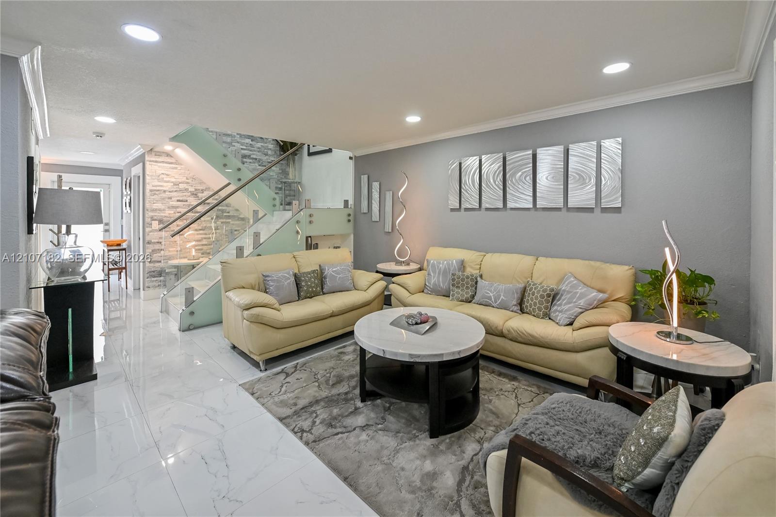 Polished porcelain tile flooring, recessed ceiling lighting, and a staircase featuring glass panels with metal railings and a textured stone accent wall Polished porcelain tile flooring, recessed ceiling lighting, and a staircase featuring glass panels with metal railings and a textured stone accent wall
