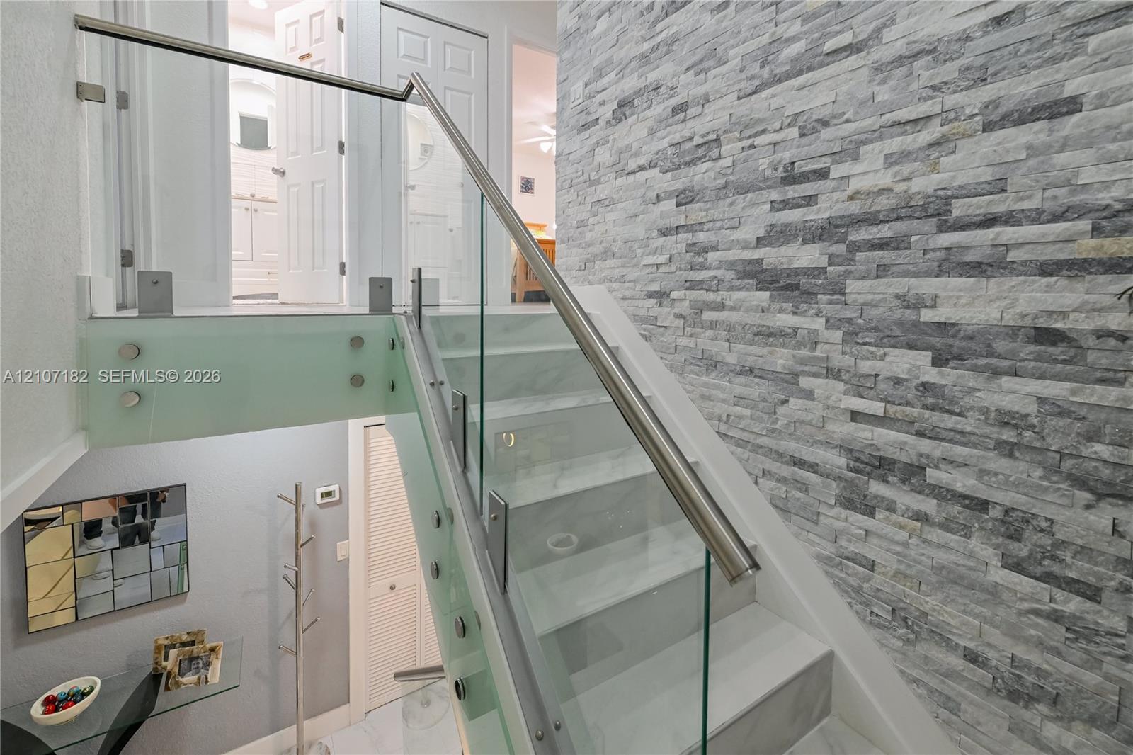 Staircase featuring stacked stone accent wall, glass panel railings, metal handrails, and solid-surface treads