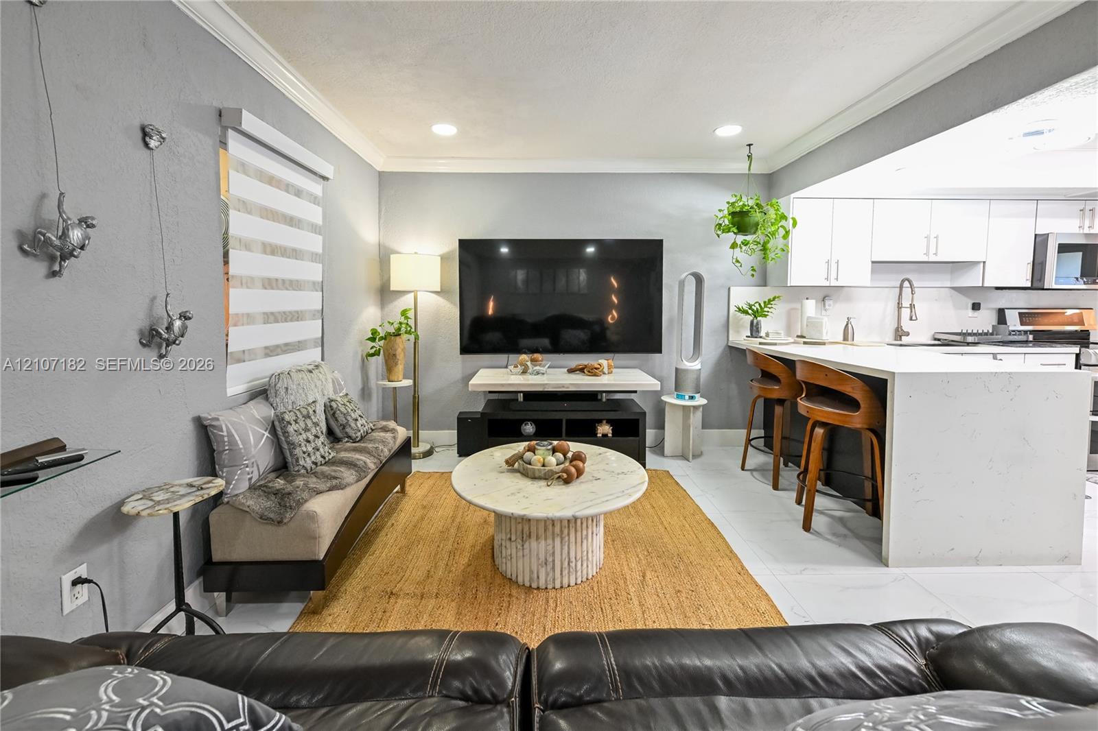 Open-concept area featuring recessed ceiling lighting, crown molding, white shaker-style cabinetry, a stone-finish waterfall edge kitchen island, and tile flooring