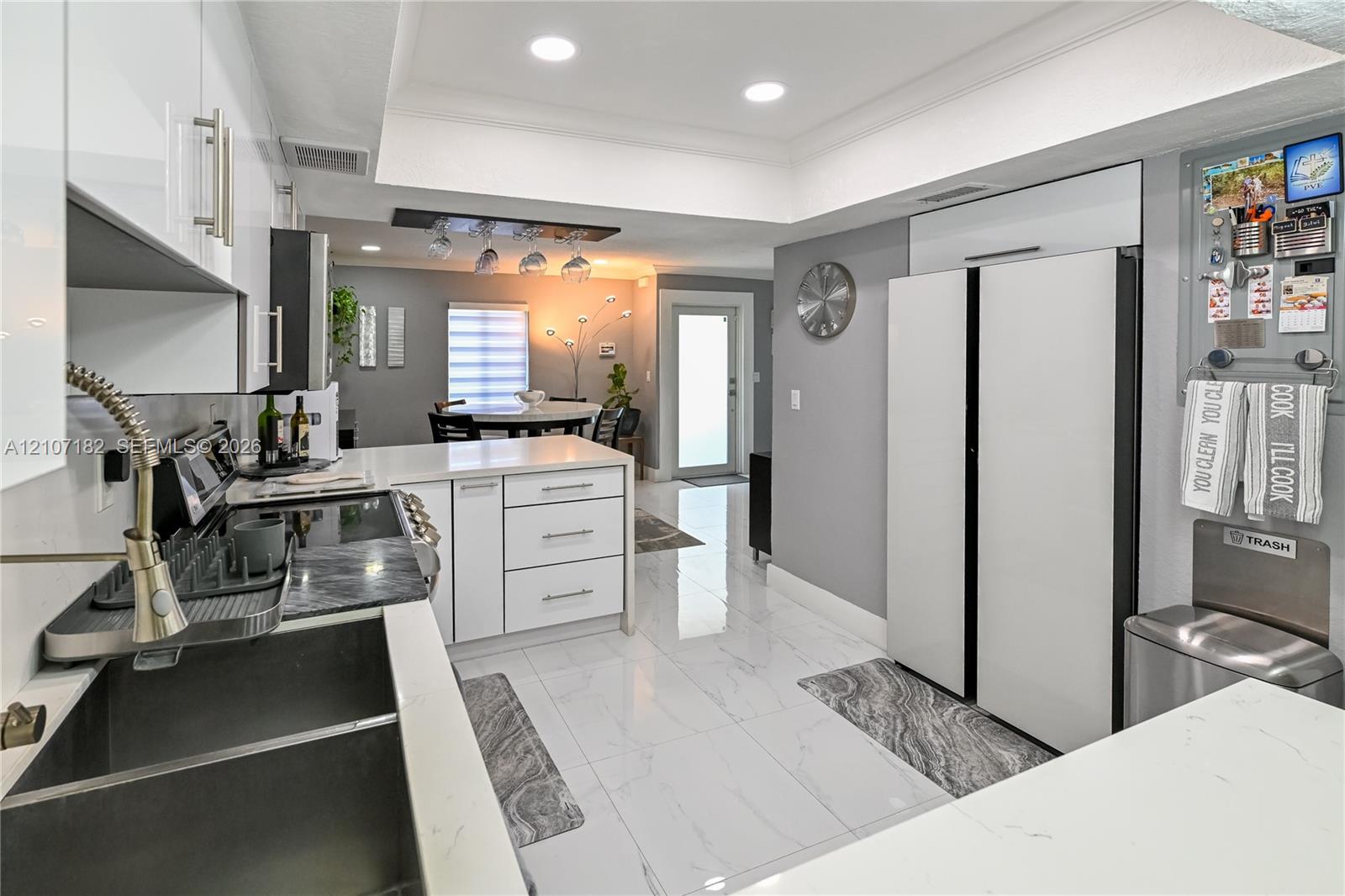 Kitchen featuring white gloss cabinetry, stone-finish countertops, large-format tile flooring, recessed lighting, and a dual-basin undermount sink with a high-arc pull-down faucet
