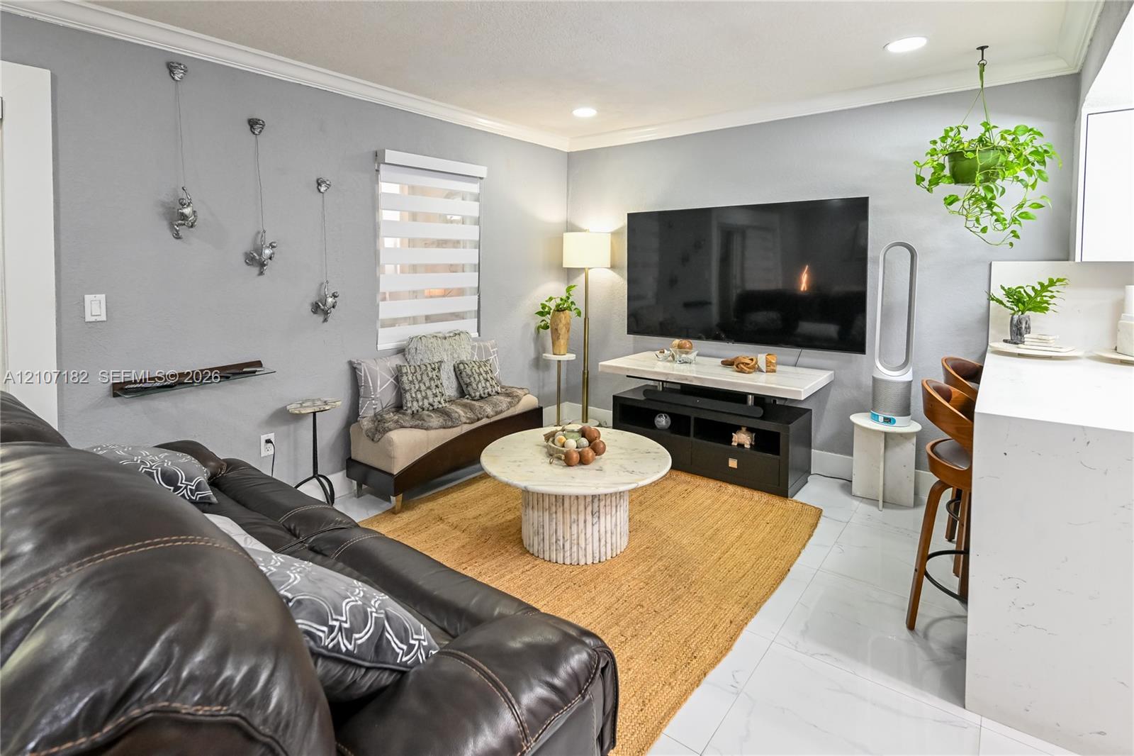 Living space featuring large-format tile flooring, crown molding, recessed lighting, and a kitchen peninsula with stone-finish countertops