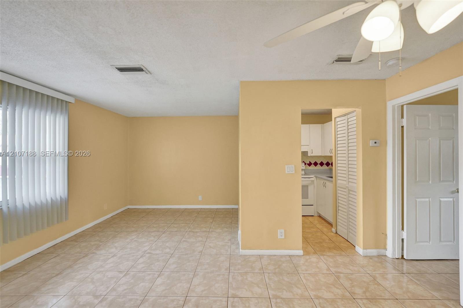 Interior space featuring neutral-toned walls, tile flooring, vertical window blinds, a ceiling fan with light fixture, and louvered closet doors