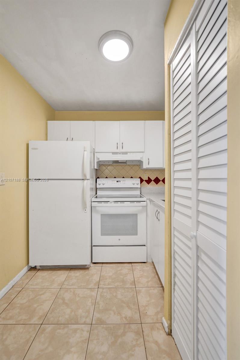 Kitchen featuring white cabinetry, an electric range, a top-freezer refrigerator, tiled flooring, and louvered bi-fold doors