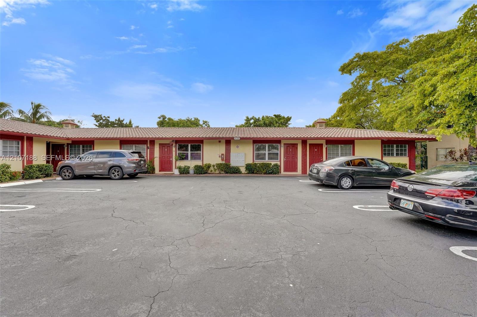 Single-story exterior featuring a low-pitch tile roof, painted stucco facade, red entry doors, and dedicated asphalt parking