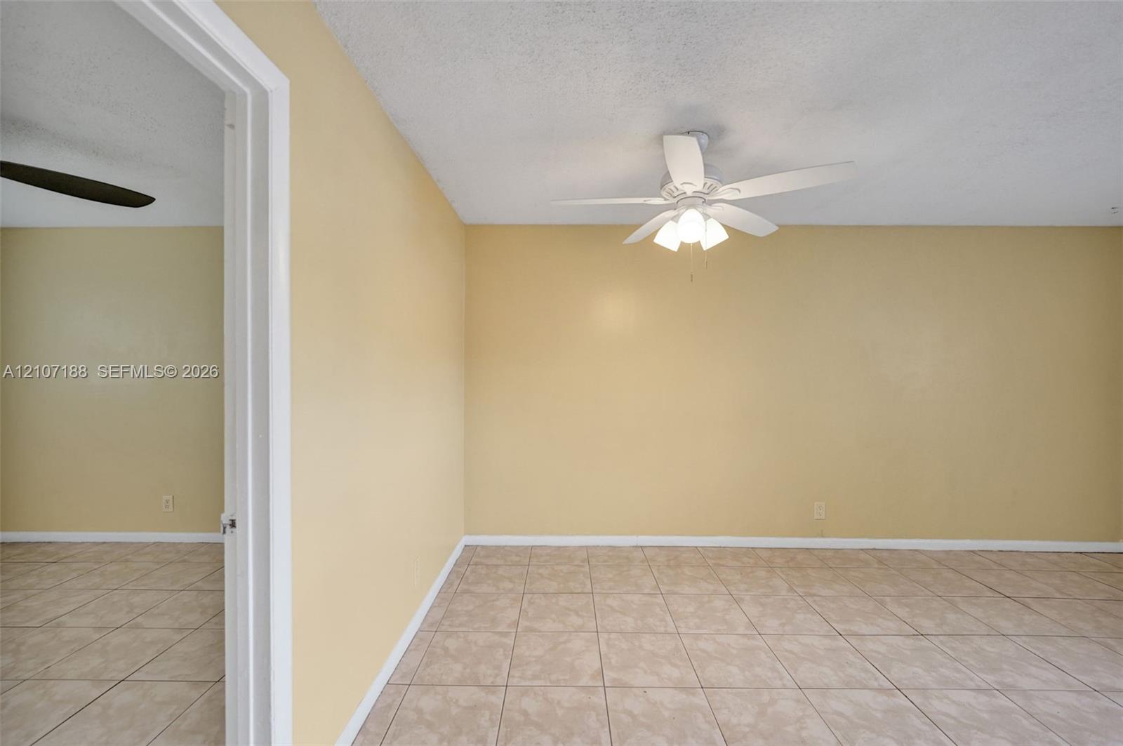 Room featuring ceramic tile flooring, a center-mounted ceiling fan with integrated lighting, and a white door frame