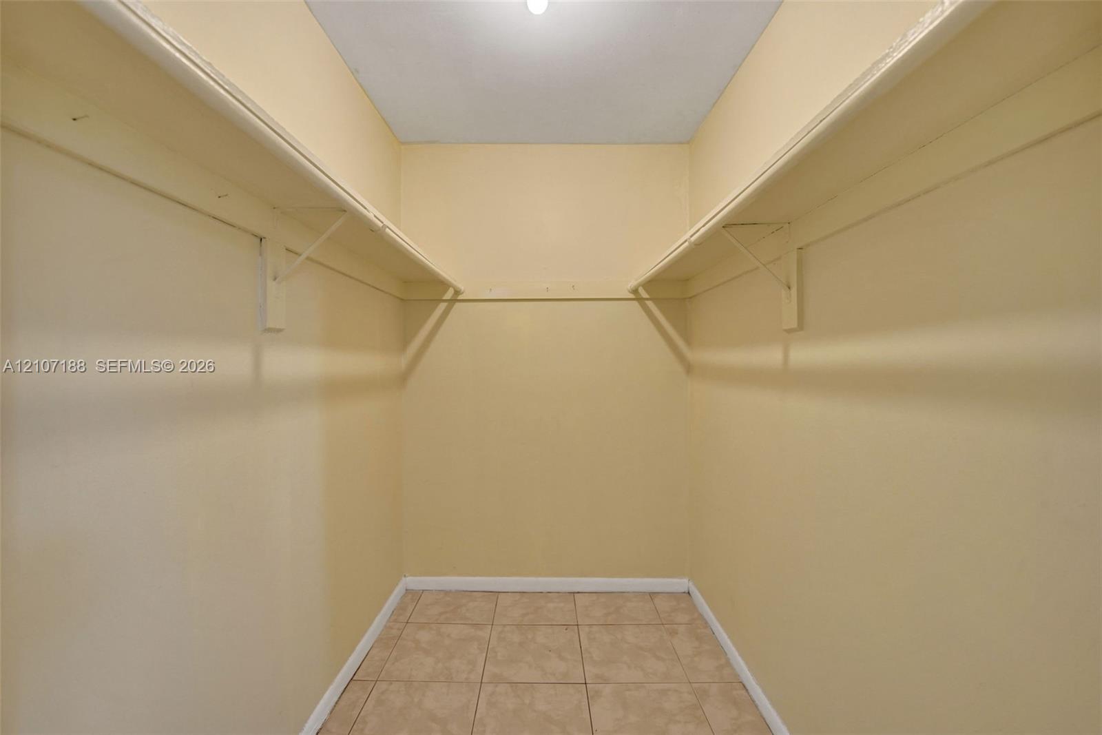 Walk-in storage space featuring built-in shelving, hanging rods, and tile flooring