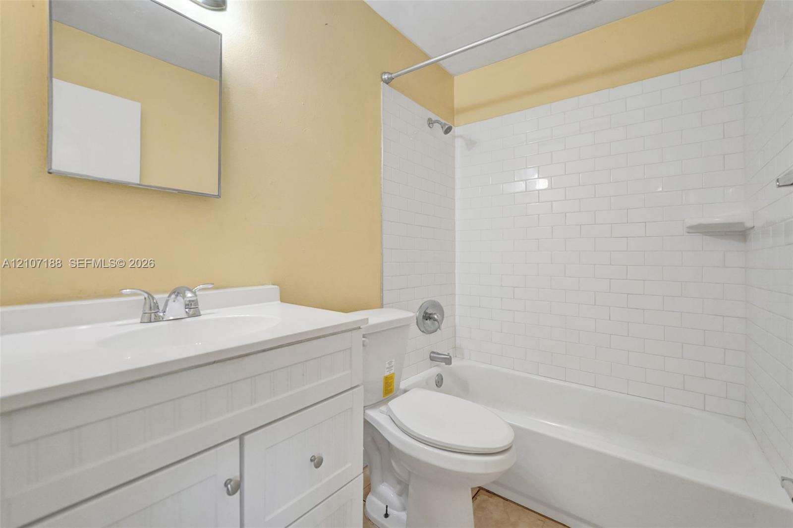 White vanity featuring a cabinet base, integrated basin, and polished chrome faucet, complemented by a subway-tiled tub enclosure and wall-mounted vanity mirror