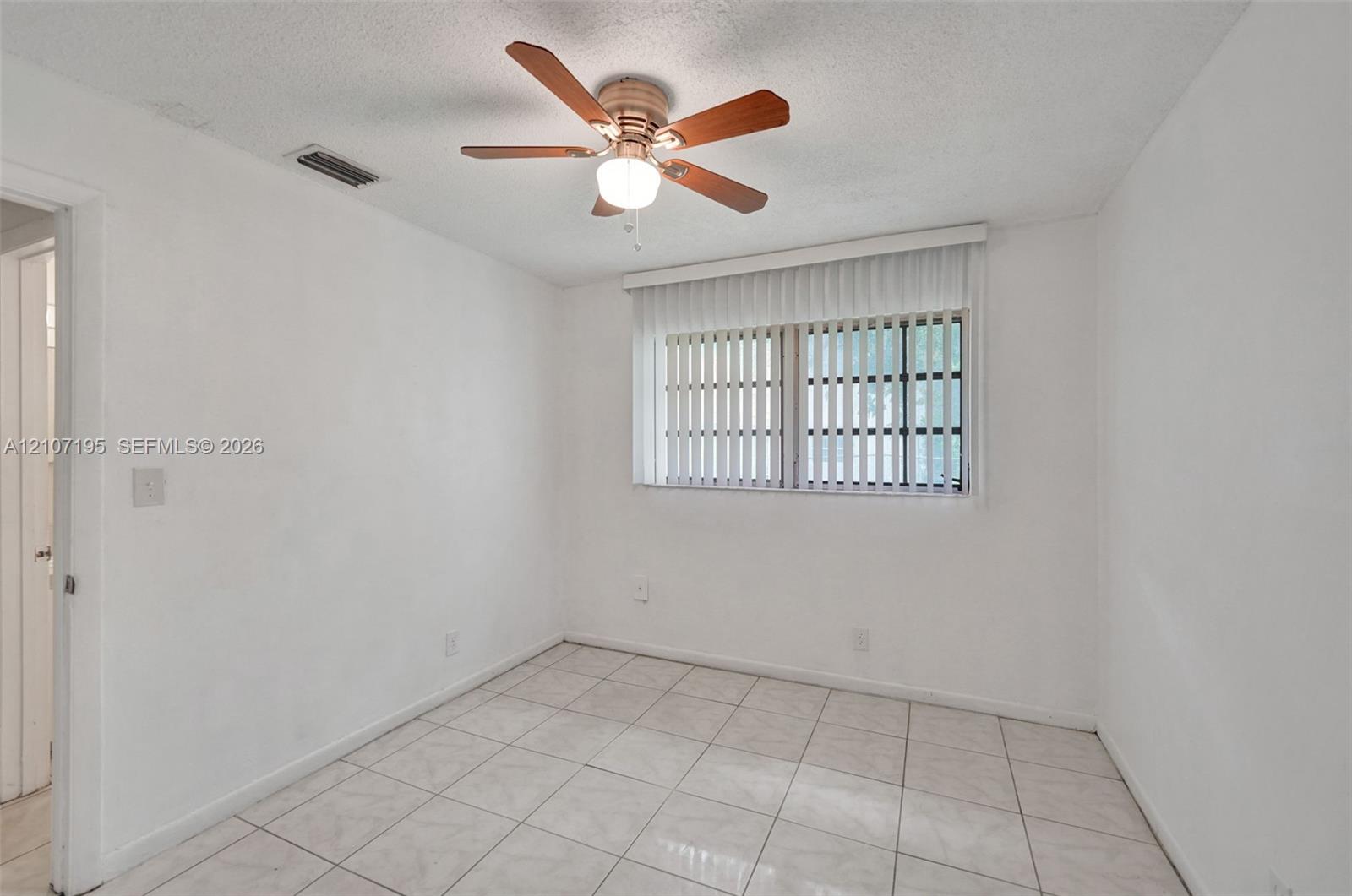 Room interior featuring neutral tile flooring, a multi-blade ceiling fan with integrated lighting, and vertical window blinds