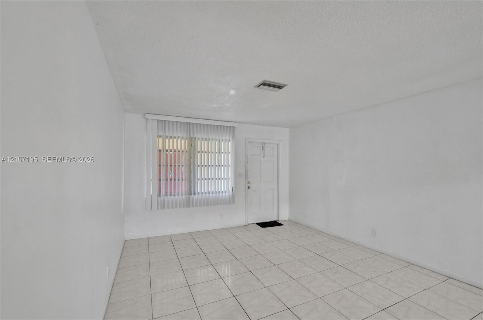 Interior space featuring light-toned ceramic tile flooring, vertical window blinds, and a solid-panel door