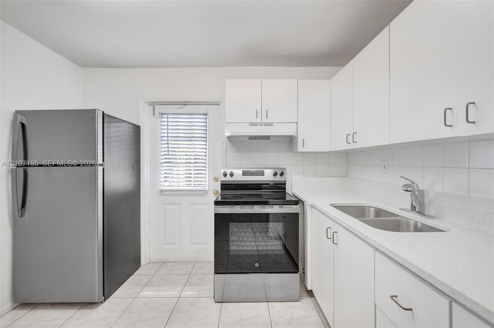 Kitchen featuring white cabinetry, solid-surface countertops, stainless steel appliances, tile backsplash, and ceramic tile flooring