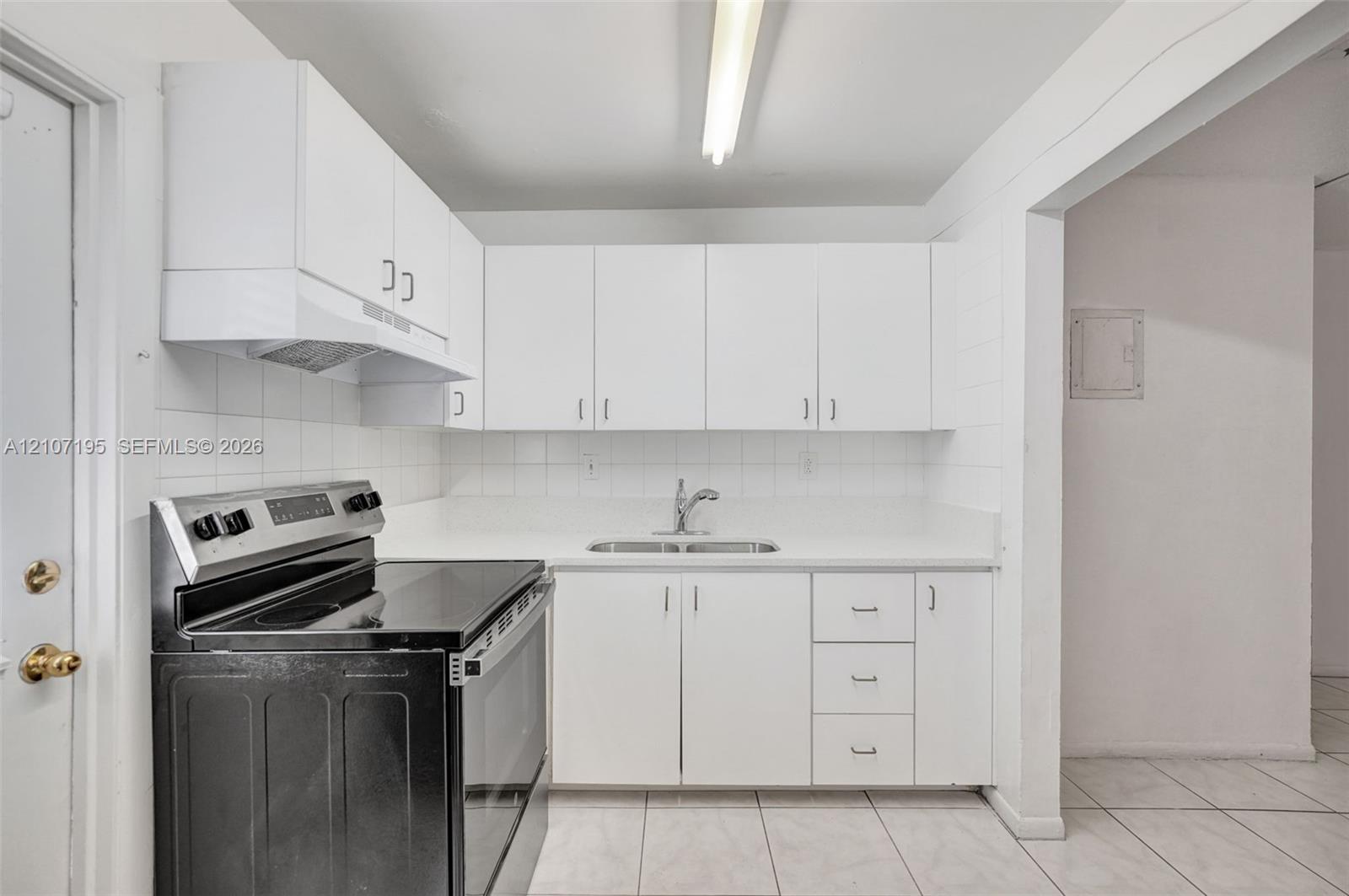 Kitchen featuring white cabinetry, solid-surface countertops, dual-basin stainless steel sink, tile backsplash, and a black electric range
