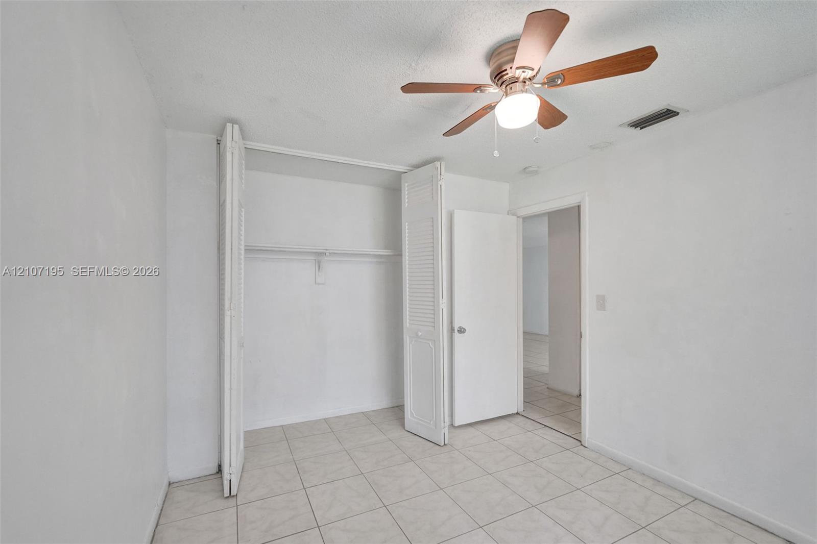 Room featuring light-colored tile flooring, a multi-blade ceiling fan with integrated lighting, and a closet with bifold louvered doors