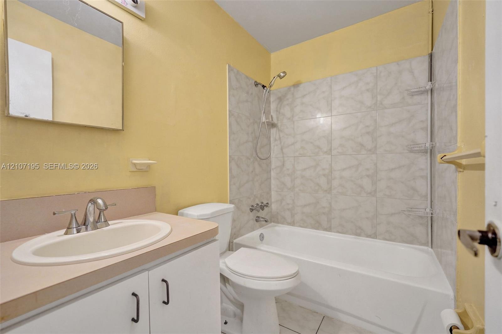 Bathroom featuring a white vanity cabinet with a solid surface countertop, integrated sink with chrome faucet, tub-shower combination with tile surround, and a wall-mounted mirror