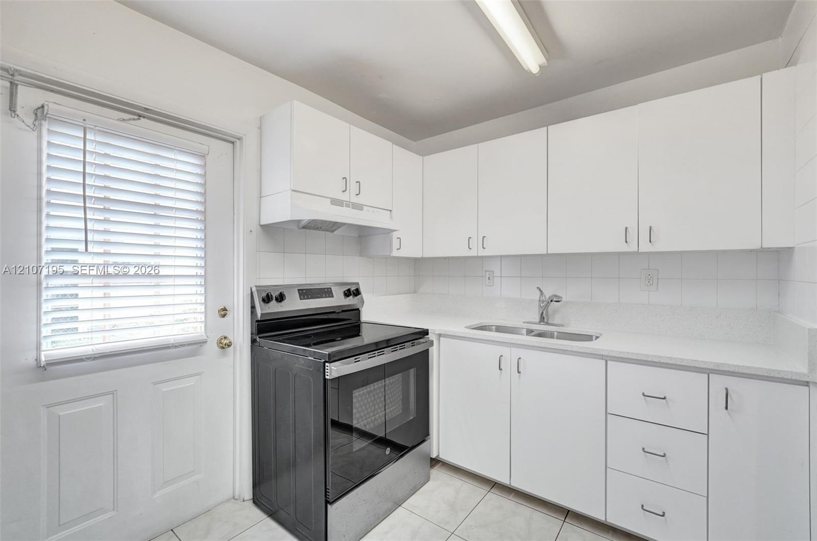 Kitchen featuring white cabinetry, light-toned countertops, tile backsplash, stainless steel range, and dual-basin stainless steel sink