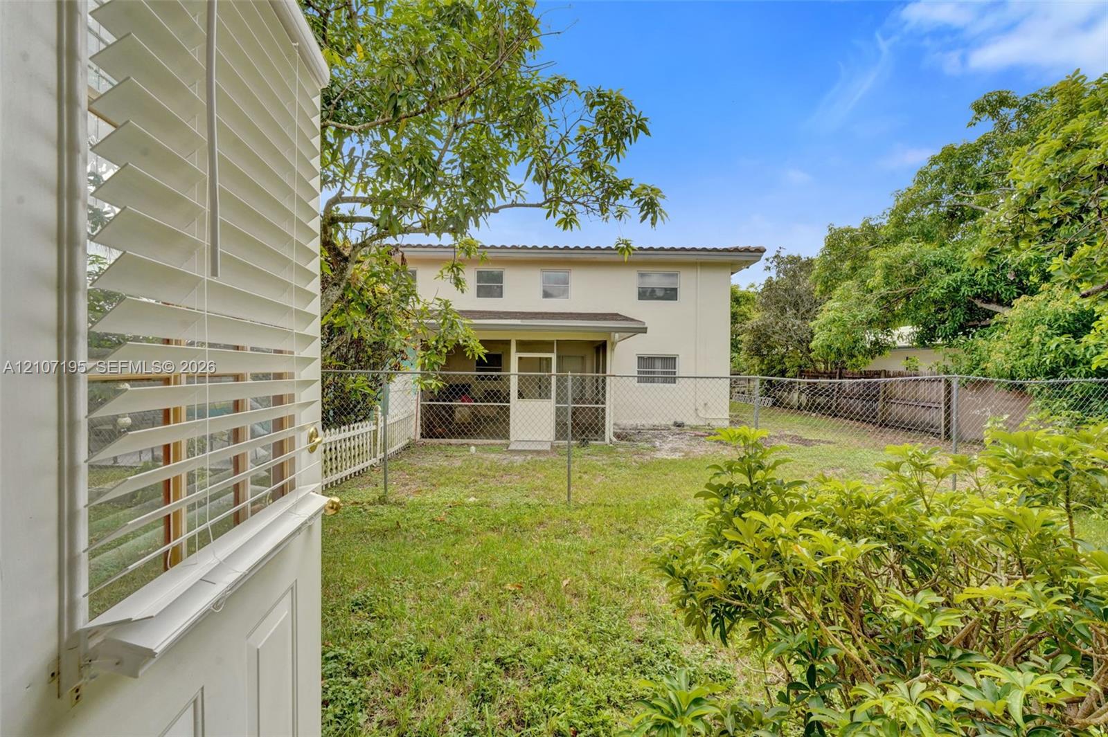 Backyard featuring a grass lawn, chain-link fencing, mature trees, and a screened-in rear porch