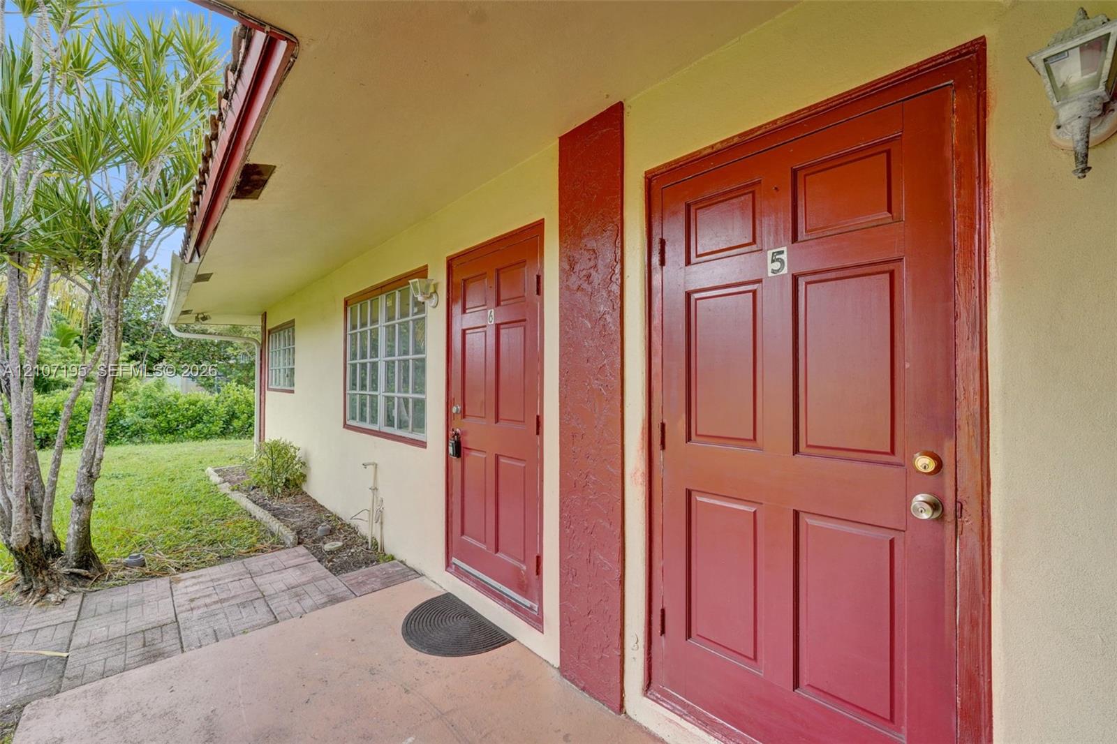 Exterior walkway featuring a concrete patio, six-panel solid core doors, glass block windows, and wall-mounted exterior light fixtures