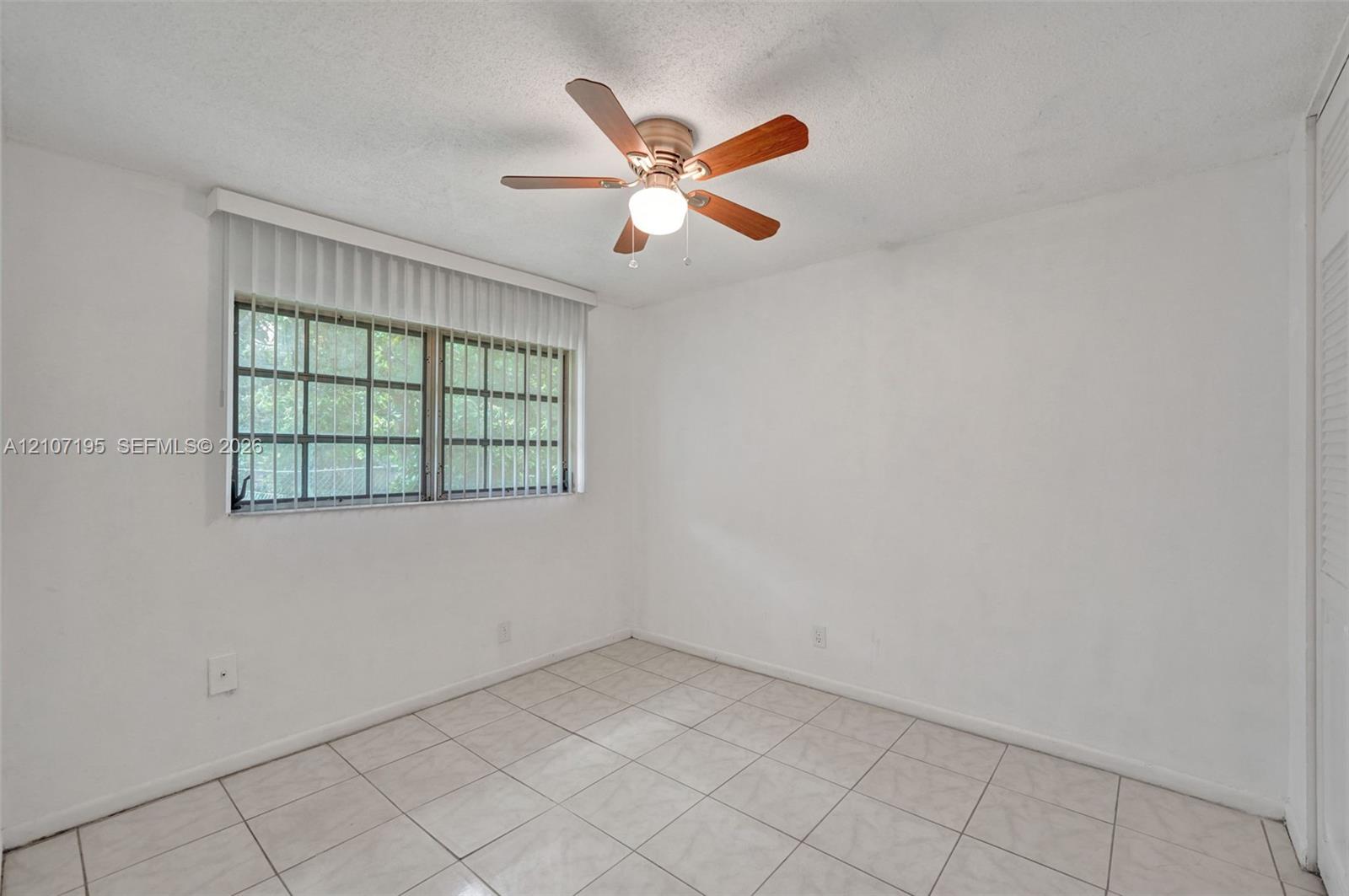 Room featuring white tile flooring, ceiling fan with light fixture, window with grid pattern, and vertical blinds