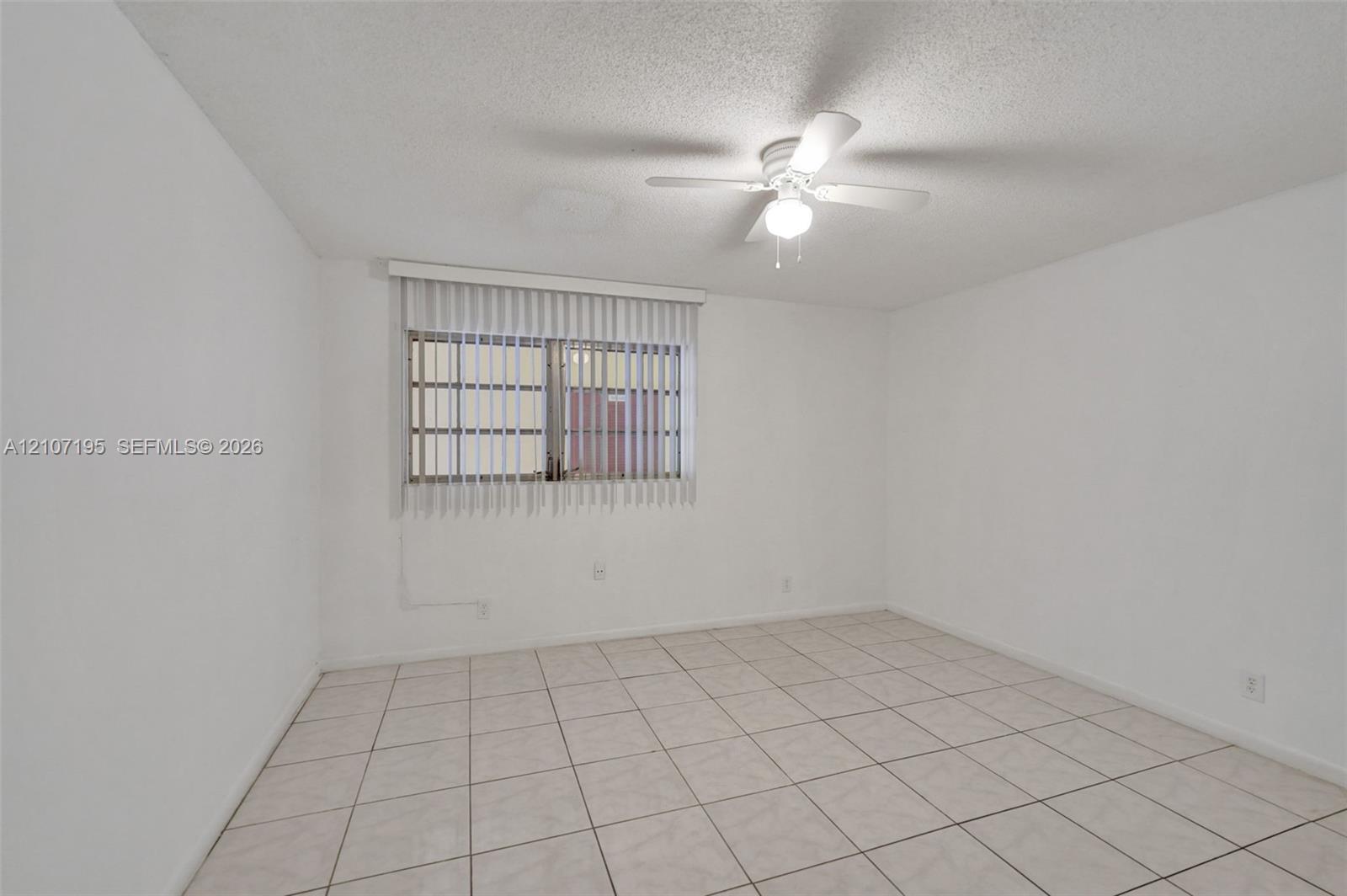 Neutral-toned tile flooring, ceiling fan with integrated lighting, and vertical window blinds