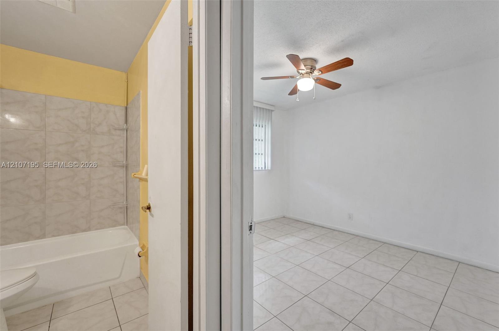 Bathroom featuring a tile-surround bathtub and neutral wall finishes, paired with an interior space highlighted by ceramic tile flooring, a ceiling fan with integrated lighting, and a vertical blind window treatment