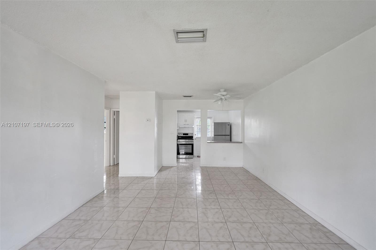 Open-concept interior featuring neutral tile flooring, white wall finishes, and a pass-through opening to the kitchen