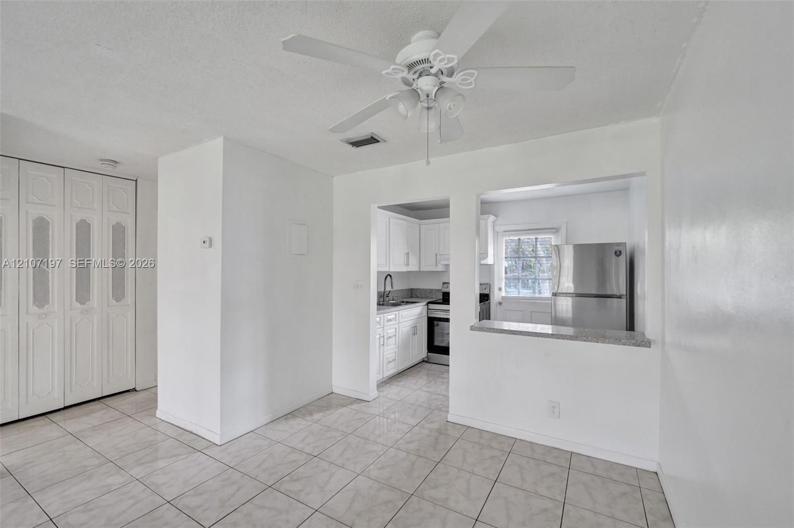 Tiled flooring, ceiling fan with light fixture, floor-to-ceiling bi-fold closet doors, and pass-through window with a stone-finish countertop