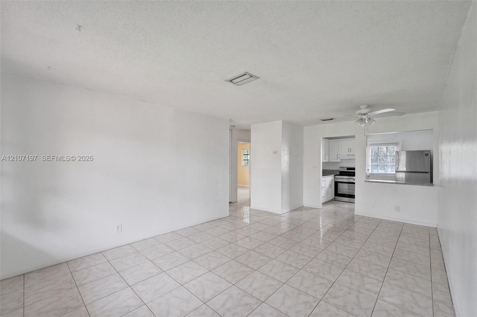Interior space featuring neutral wall tones, ceramic tile flooring, ceiling fan with integrated lighting, and a kitchen pass-through