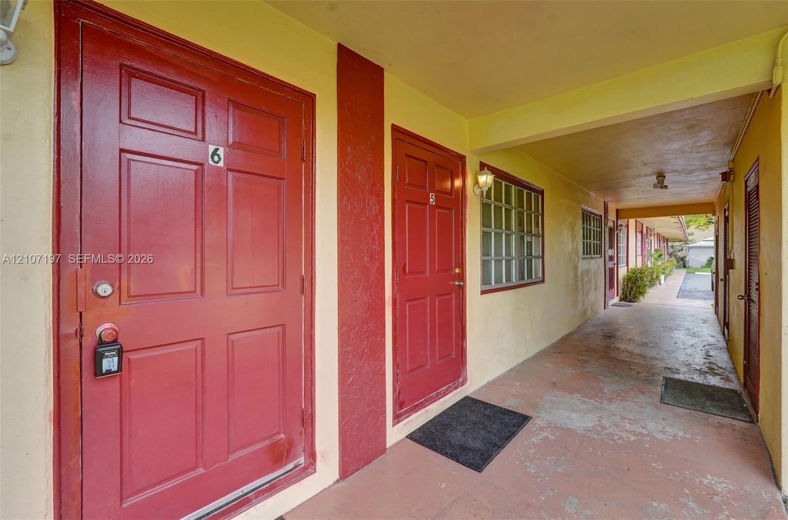 Covered exterior corridor featuring painted paneled doors, wall-mounted light fixtures, and multi-pane grid windows