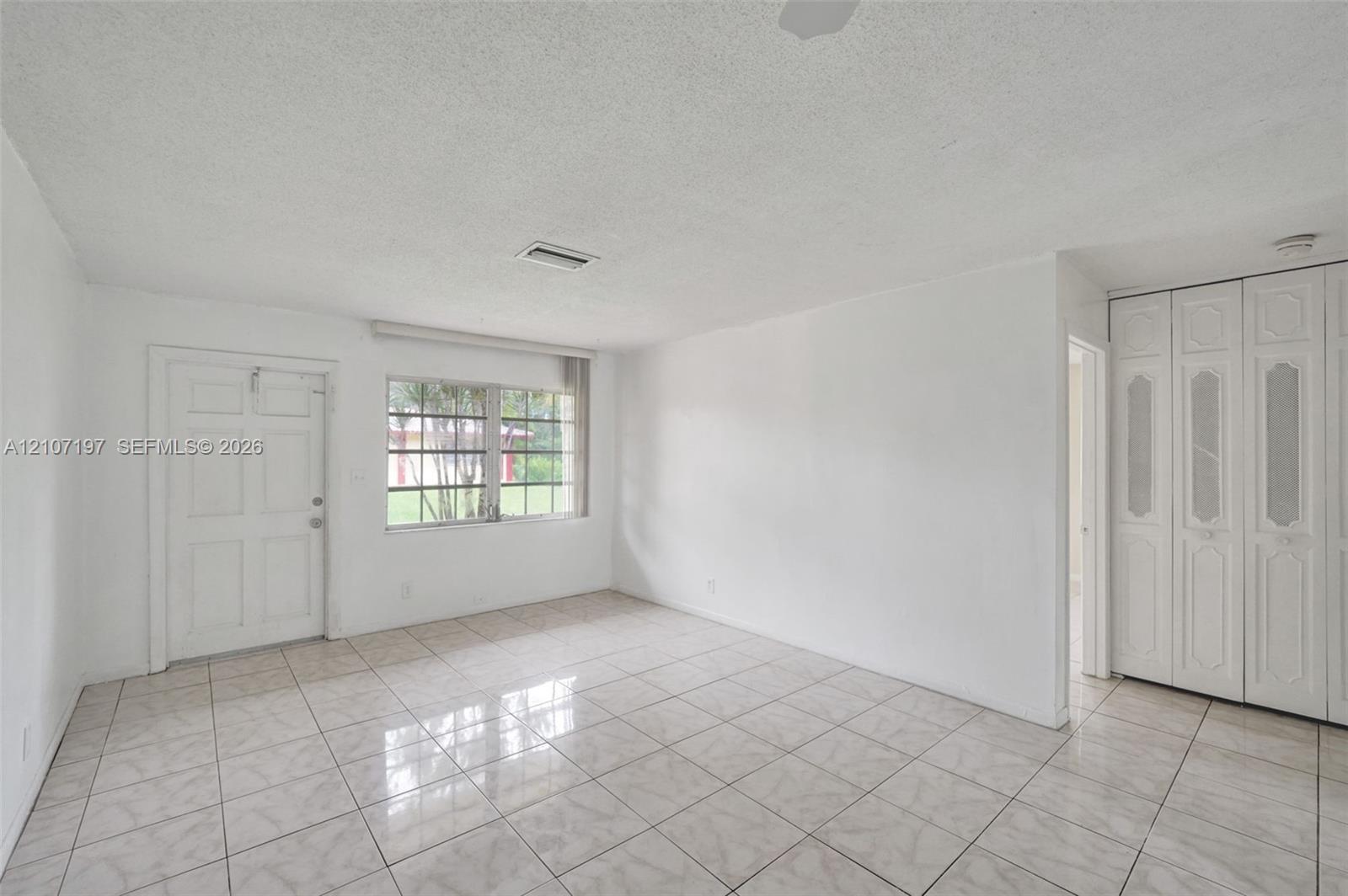 Ceramic tile flooring, white paneled entry door, multi-pane window, and floor-to-ceiling built-in closet with decorative paneling