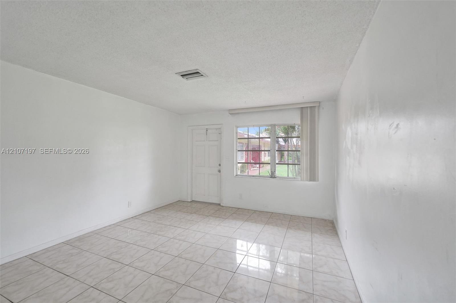 Interior space featuring large-format neutral floor tiling, textured ceiling finish, and a multipane window with vertical blinds