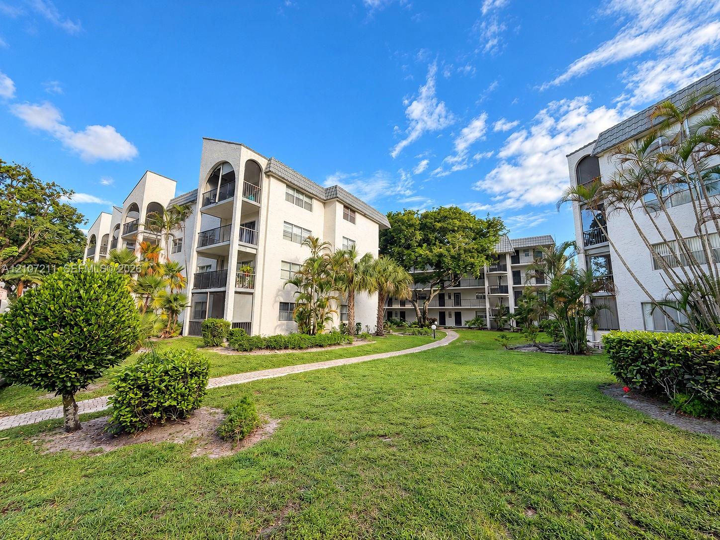 Multi-story exterior featuring arched architectural detailing, private balconies with metal railings, a paved pedestrian pathway, and mature landscaping