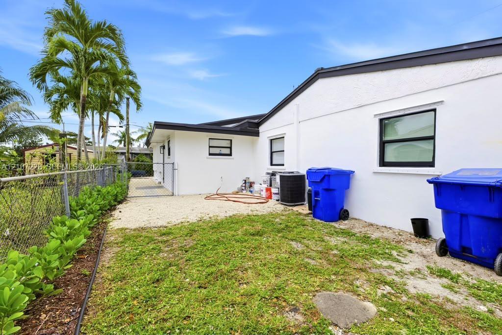 Exterior side yard featuring white stucco siding, dark-trimmed windows, a chain-link fence, and mature palm trees