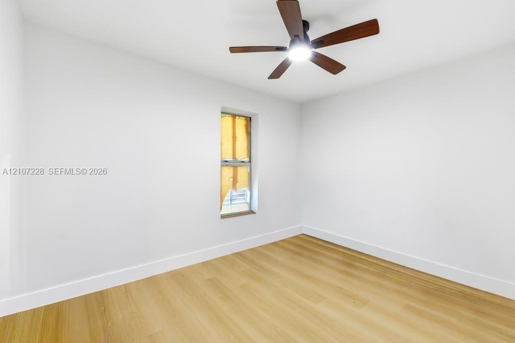 Room featuring wood-finish flooring, white walls, and a ceiling fan with integrated lighting