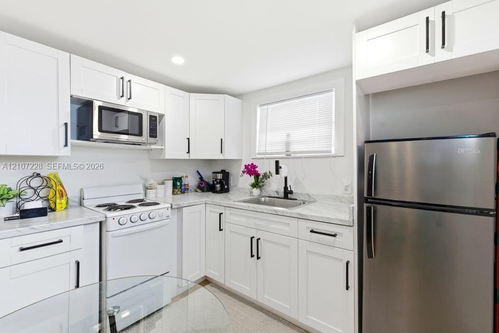 Kitchen featuring white Shaker-style cabinetry, stone-patterned countertops, stainless steel appliances, and a matte black gooseneck faucet