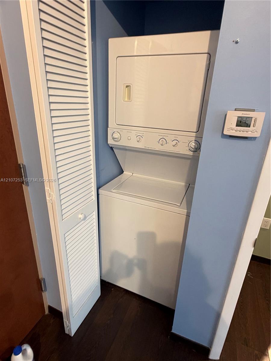 Stackable laundry unit with white finish, louvered bi-fold closet door, and digital wall-mounted thermostat
