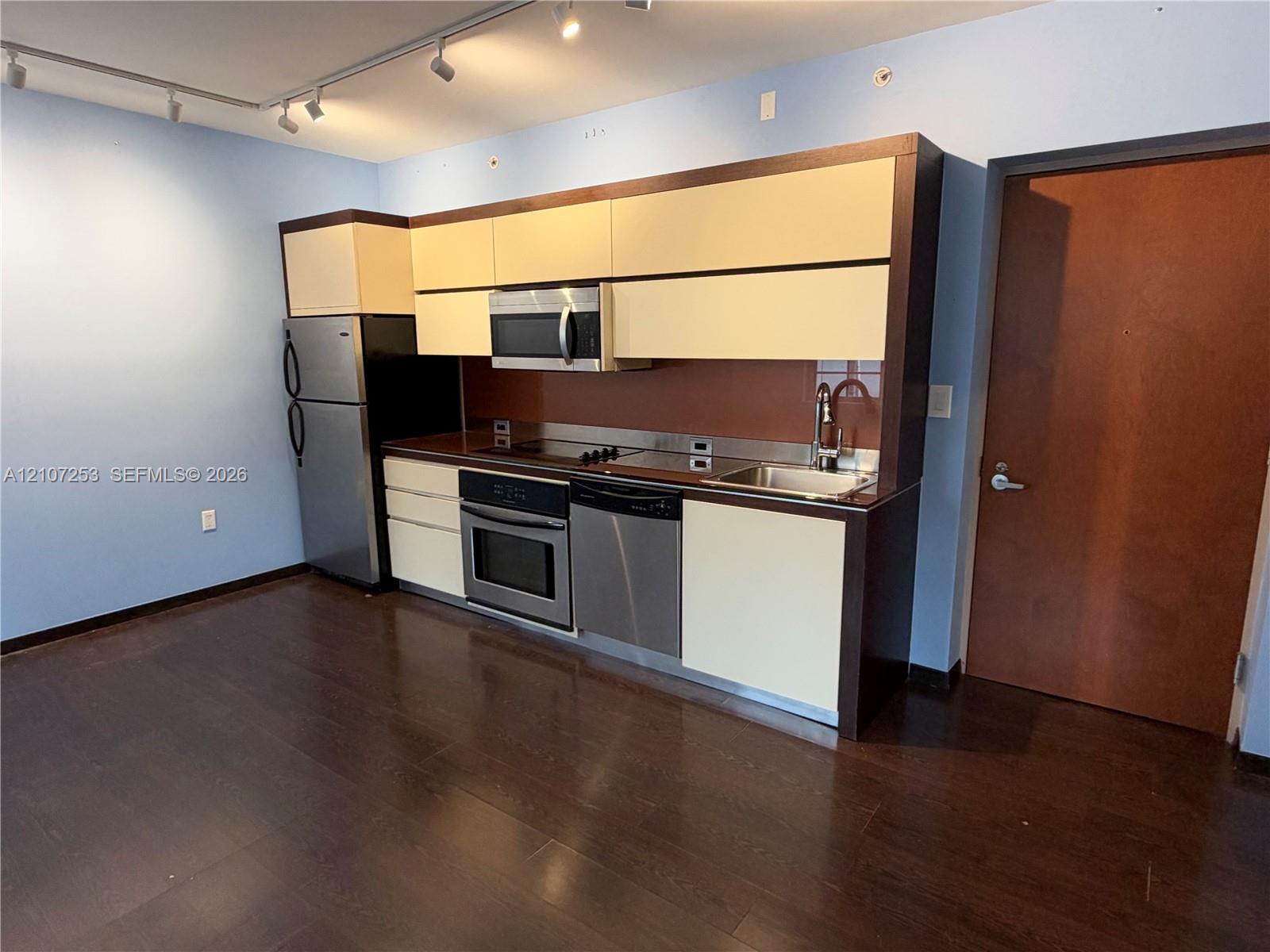 Kitchen featuring stainless steel appliances, flat-panel cabinetry, a solid-surface backsplash, and wood-finish flooring with ceiling-mounted track lighting