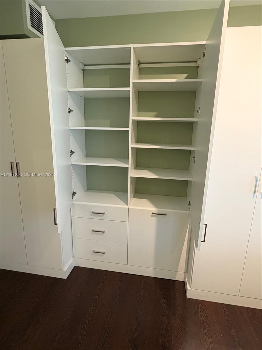 Custom built-in white cabinetry featuring adjustable shelving, integrated storage drawers, hanging rods, and sleek metallic hardware over wood-finish flooring