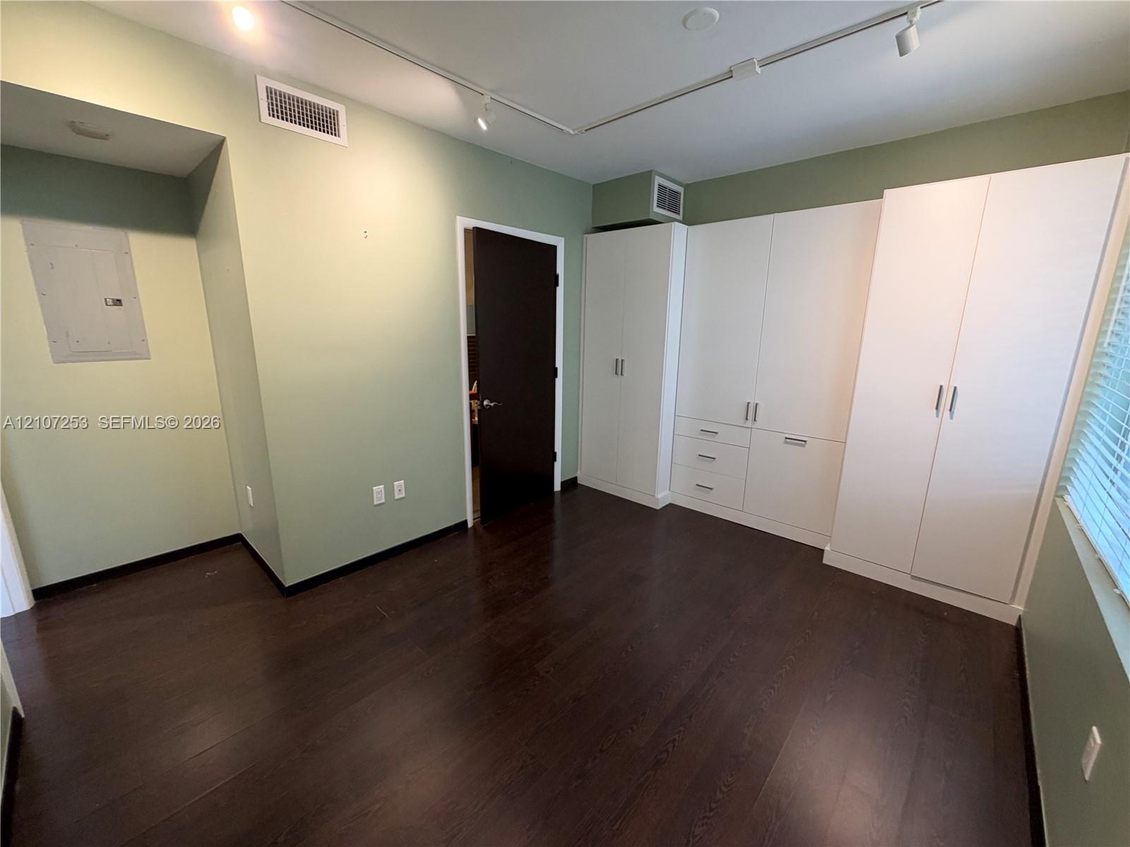 Dark wood-finish flooring complemented by white, built-in floor-to-ceiling cabinetry featuring integrated drawers and brushed metal hardware, high-contrast door finishes, and track lighting
